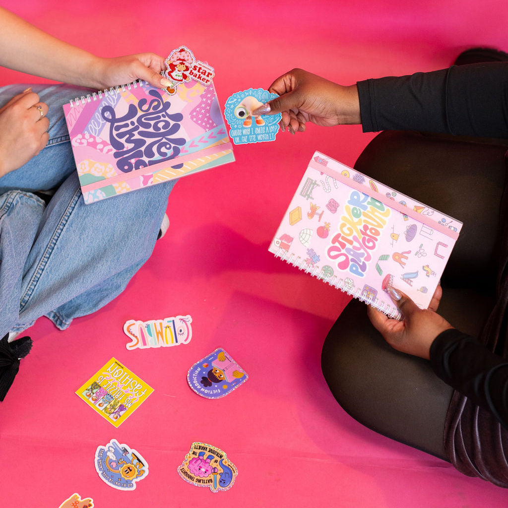 Two people sitting on a pink floor with colorful stickers and notebooks.