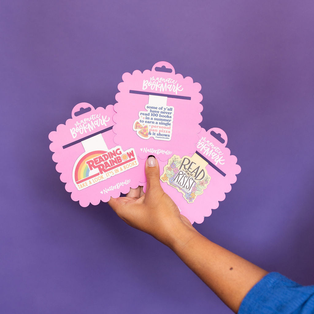 Hand holding pink bookmarks with colorful designs against a purple background