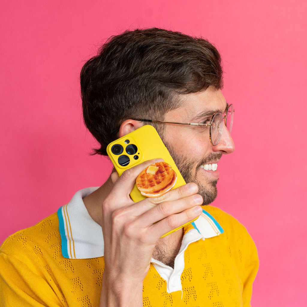Man in yellow shirt holding a phone with a waffle sticky grip on a pink background