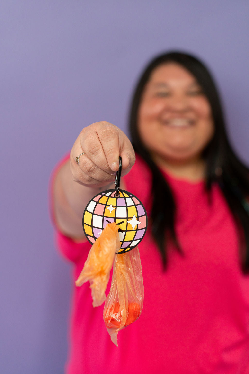 Person holding a colorful disco ball carabiner  against a purple background