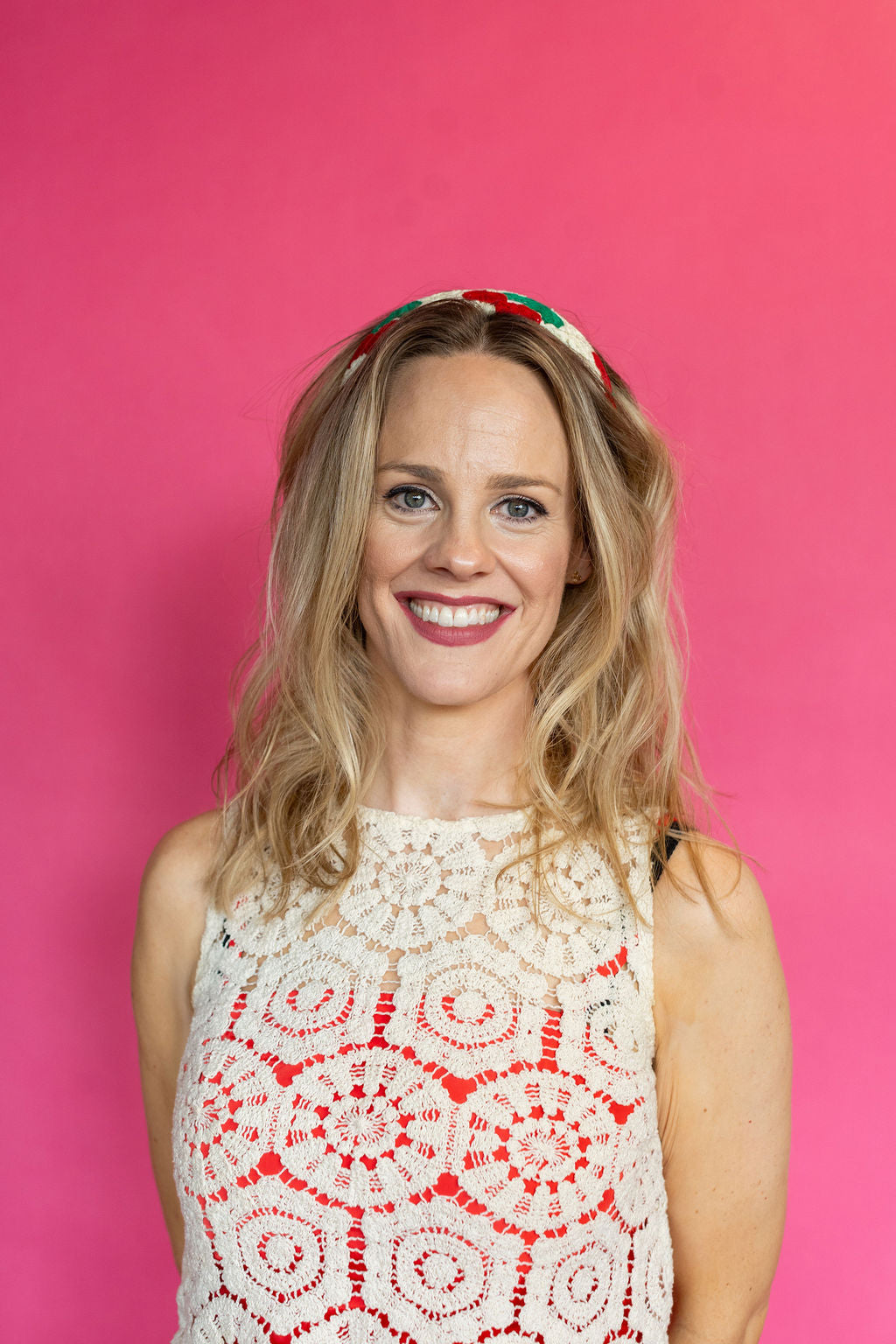 Woman wearing a white lace top with red patterns against a pink background