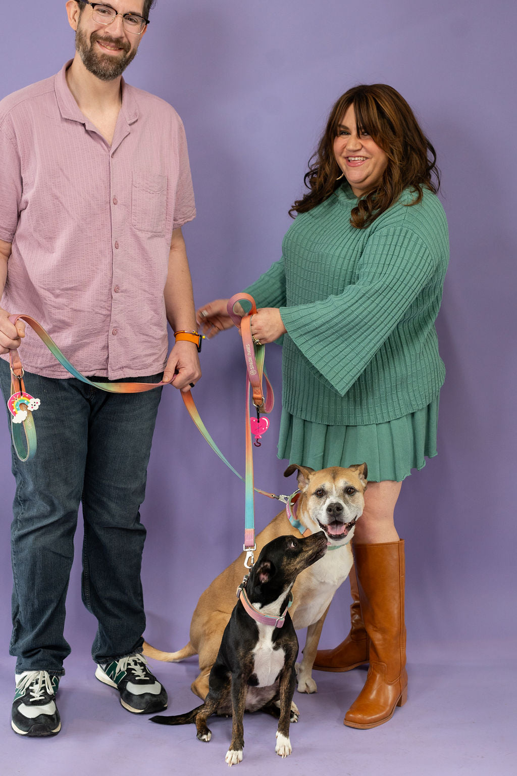 Two people with two dogs on leashes against a purple background