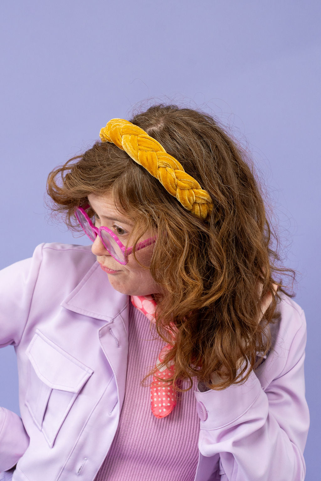 Person wearing a yellow headband, pink glasses, and a pink outfit against a purple background